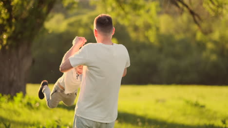 Loving-young-father-and-son-play-on-the-grass-in-the-summer-at-sunset-in-slow-motion.
